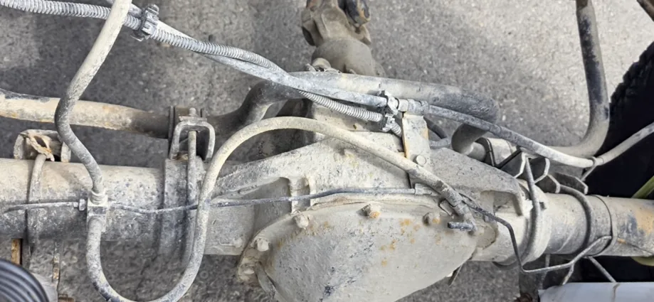 Front axle housing, differential cover, brake hoses and wiring loom coated in a heavy layer of pale road salt residue.