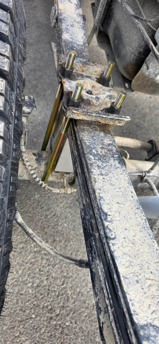 Leaf-spring hanger bracket and frame rail with new plated bolts installed, salt residue still present along the rail and tire alongside.
