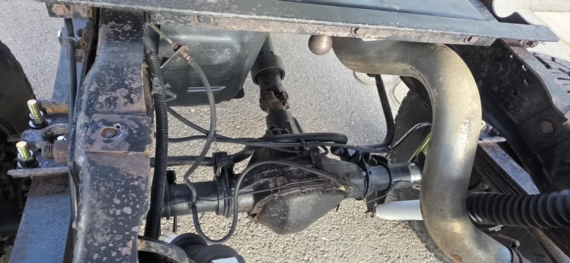 Rear axle, driveshaft, exhaust pipe and shock mounts viewed from under a truck frame, with wiring and brake lines visible.