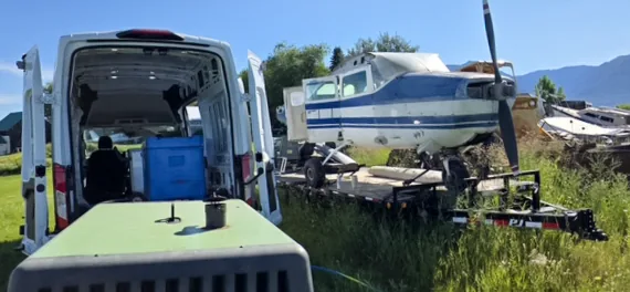 Rear doors of the Summit Cryo rig van open showing the blast unit and supply bins, parked in a grassy yard next to a boat sitting on a flatbed trailer.