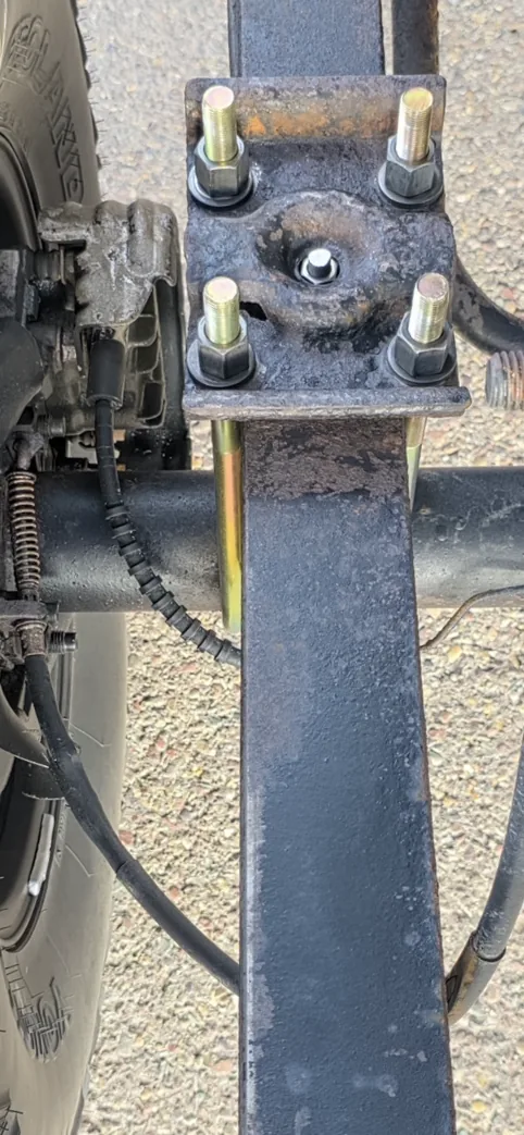 Spring hanger bracket bolted to a cleaned dark frame rail with new plated hardware, brake line and wheel visible to the side.