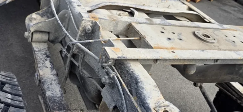 Close view of truck frame rails and a crossmember covered in dried road salt and grime, with brake lines and wiring routed alongside.